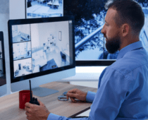 Security professional monitoring surveillance cameras on multiple screens, holding a radio while overseeing security system operations