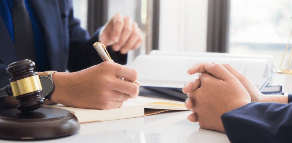Lawyer writing notes during a legal consultation, with gavel and law books on the desk in front of a client