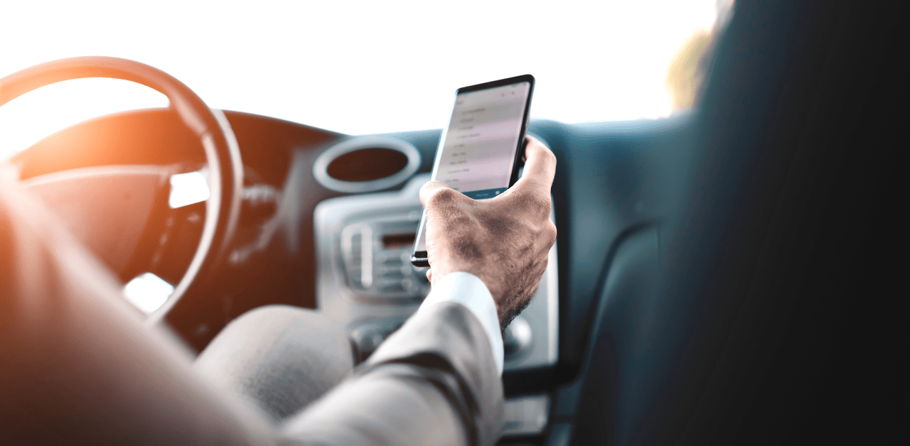 Driver uses a smartphone behind the wheel, illustrating the danger of distracted driving
