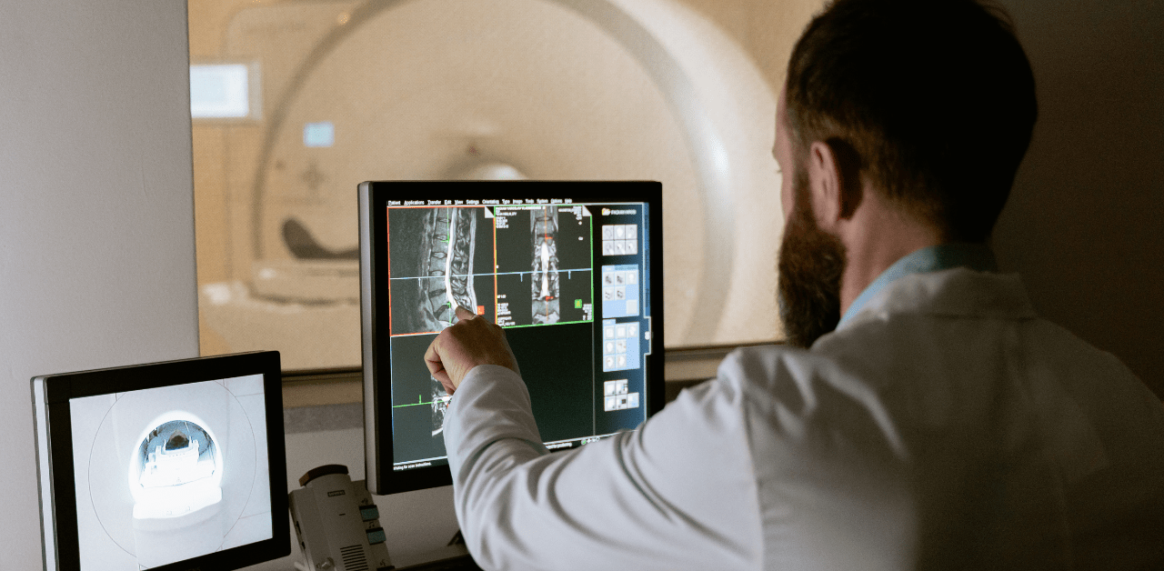 Doctor examining spinal MRI scans on a computer monitor next to an MRI machine