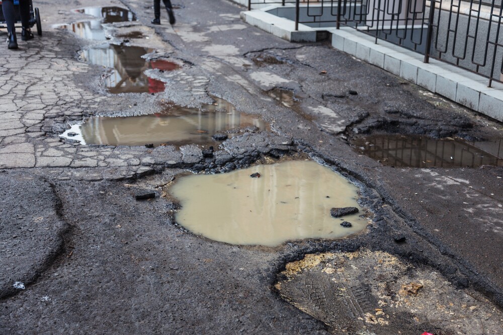 Very bad quality road with potholes. Hole in asphalt, bad asphalt. Pit, unsafe, hole road. Transportation, destruction of roads, risk of movement by car concept. Bad roads concept