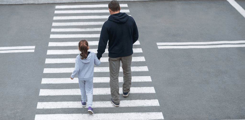 A man and a young girl holding hands as they walk across a crosswalk