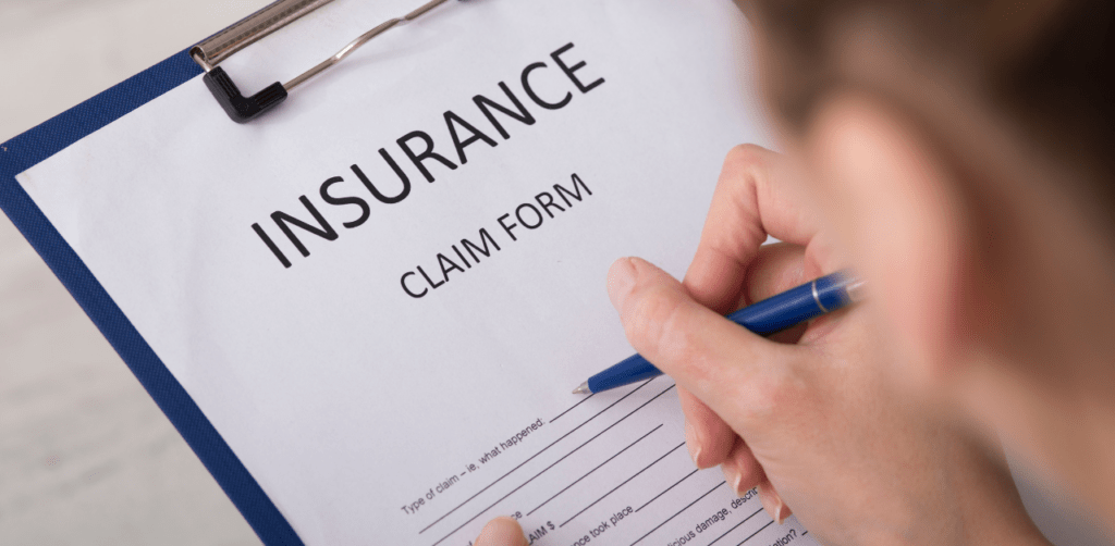 Close-up of a person filling out an insurance claim form on a clipboard with a blue pen