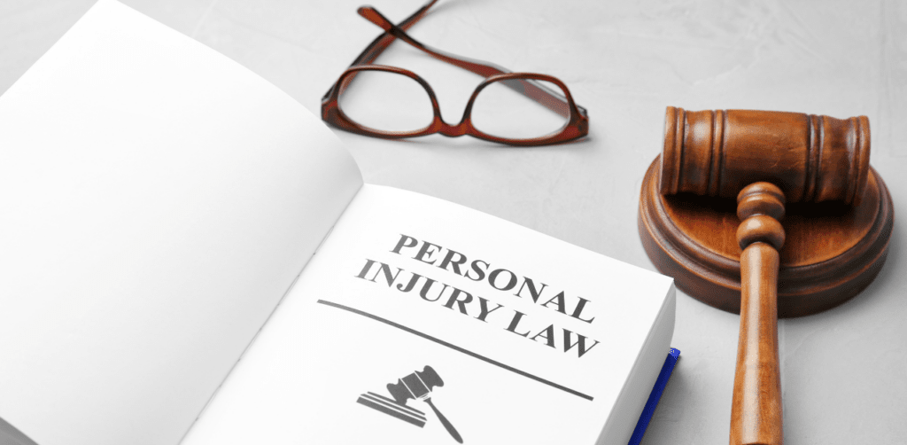 Open book titled Personal Injury Law with a gavel and eyeglasses on a gray surface in the background