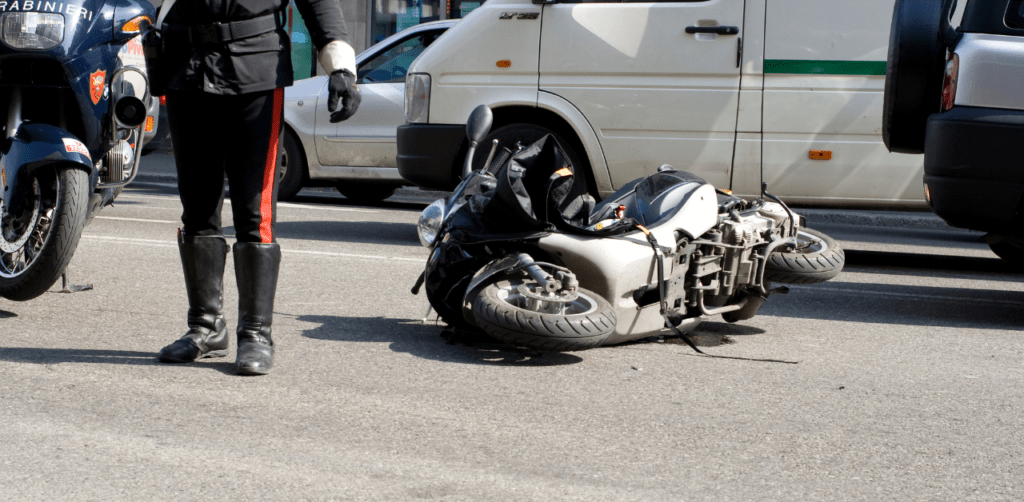 Police officer stands near an overturned motorcycle on a city street, with parked vehicles in the background