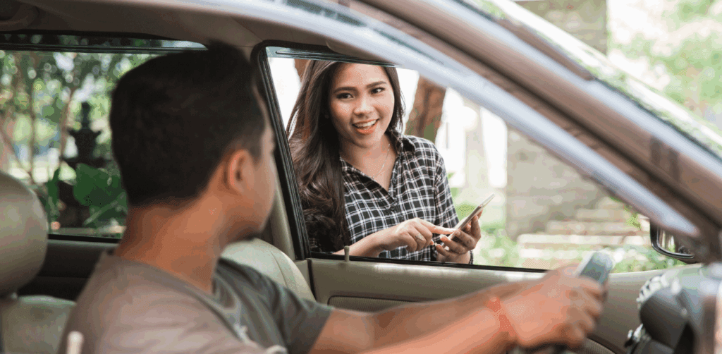 Smiling woman with phone speaks to rideshare driver through open car window during Uber pickup