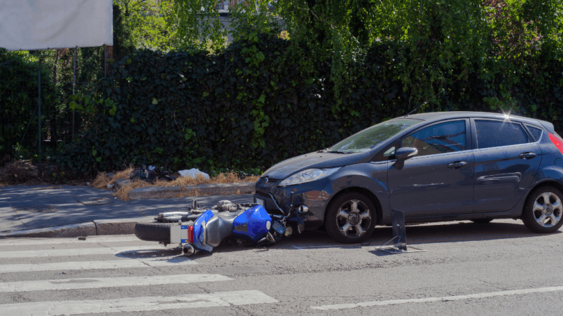 Car and fallen motorcycle after collision at intersection, illustrating road accident, vehicle damage, and traffic safety risks