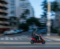 Person riding a red scooter through a city street with motion blur, representing fast urban commuting and mobility
