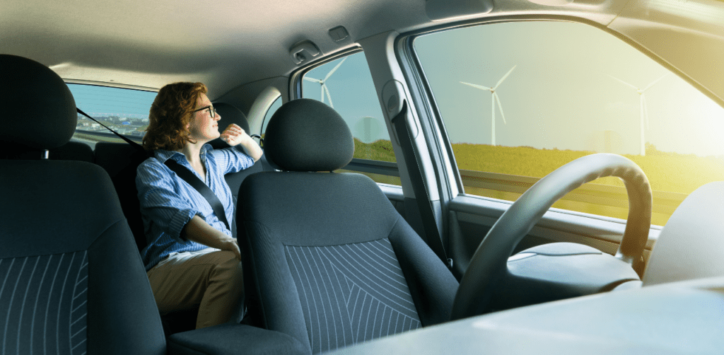 Woman seated in a car looking out the window at wind turbines, reflecting on sustainable energy during a scenic drive