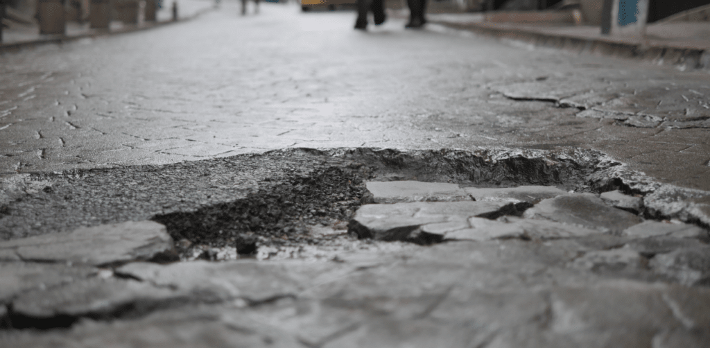 Close-up of a damaged roadway with a large pothole and broken pavement in the middle of a street