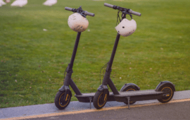 Two electric scooters with helmets hanging from the handlebars parked beside a grassy area