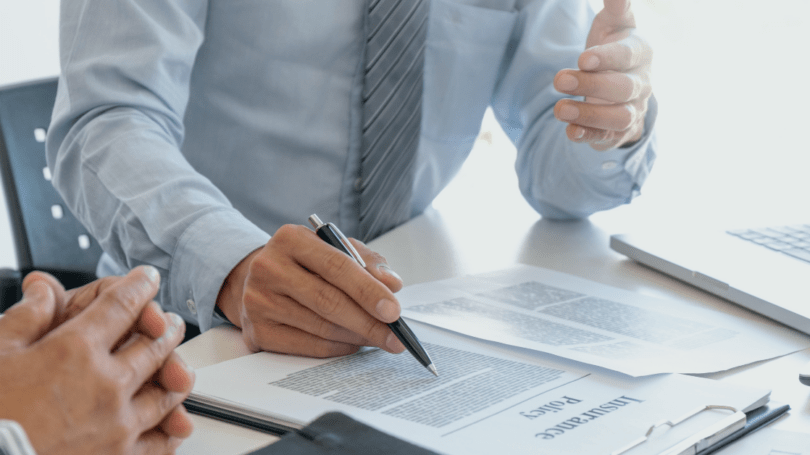 Insurance representative reviewing policy documents with a client at a desk, pointing to paperwork during a discussion about coverage or claims