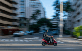 Person riding a red scooter through a city street with motion blur, representing fast urban commuting and mobility
